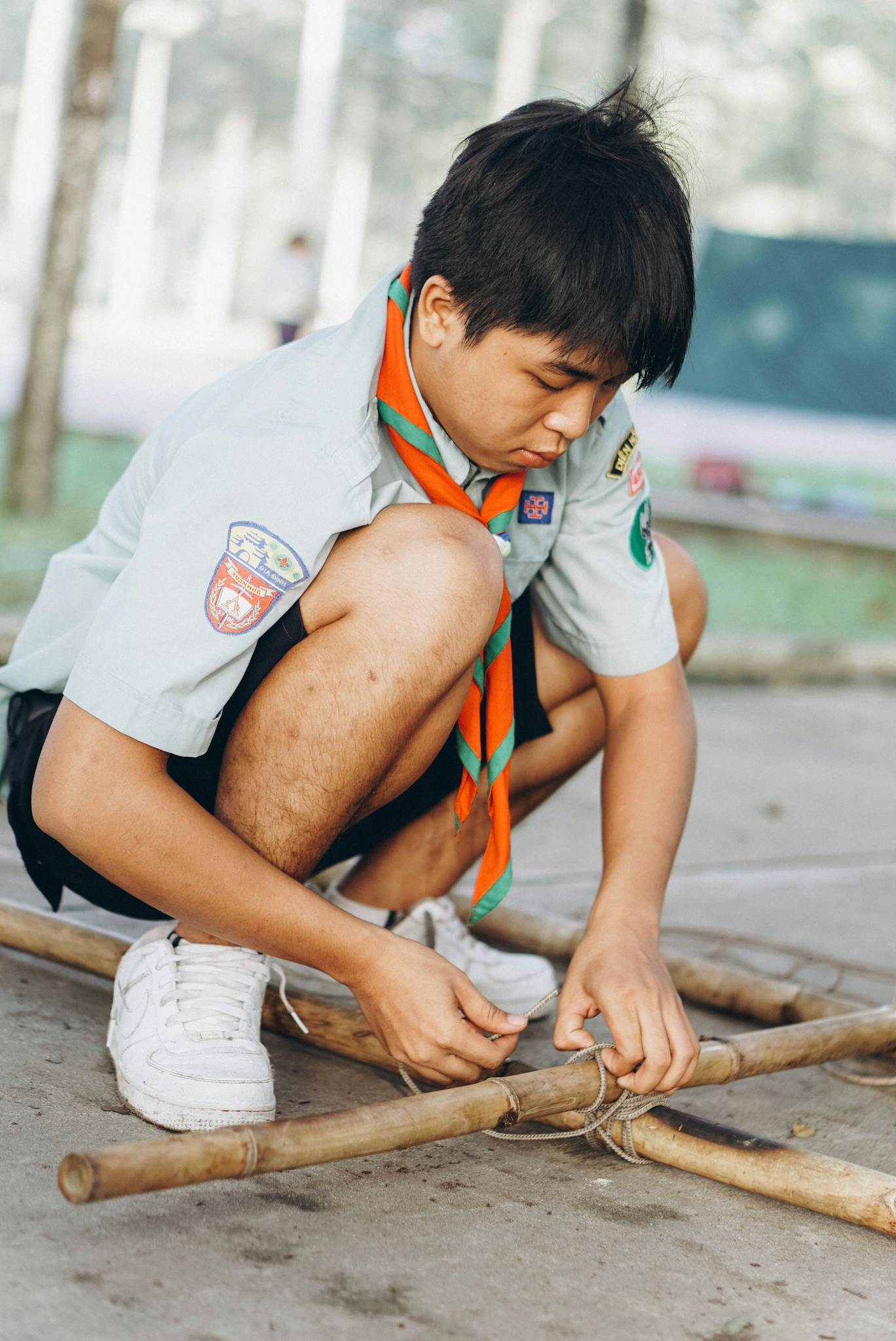 A scout tying knots on bamboo sticks during an outdoor activity, showcasing teamwork and learning.