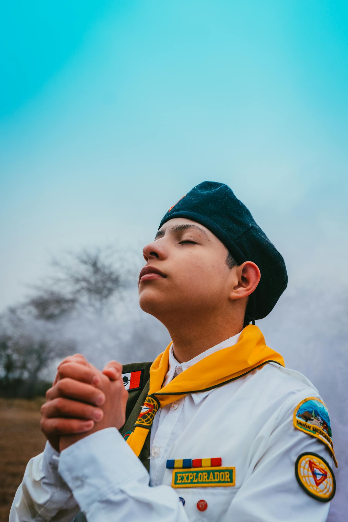 Portrait of a teenage scout in uniform with eyes closed and hands clasped, outdoors.