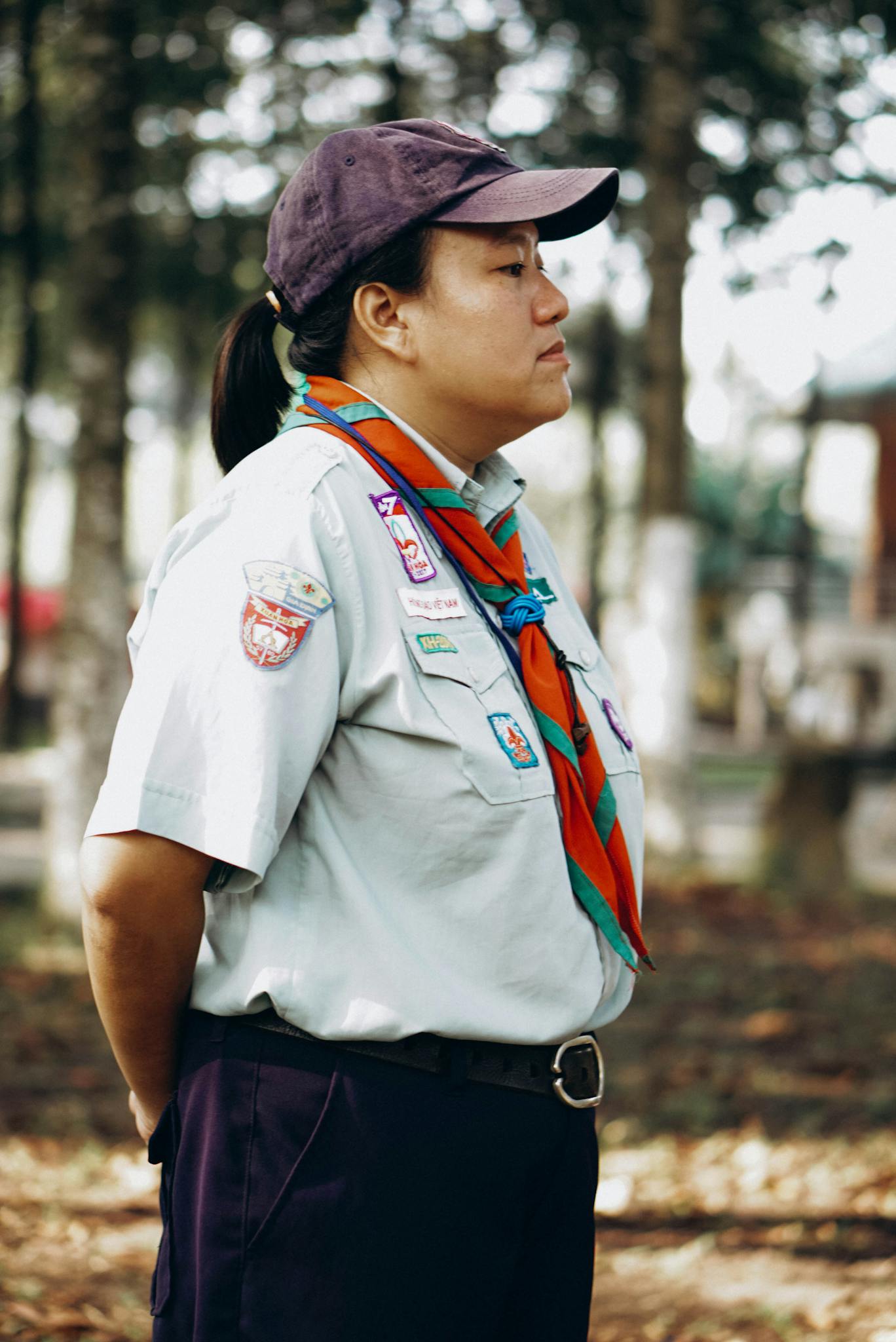 Profile of a scout leader standing in a forest, in uniform with badges.